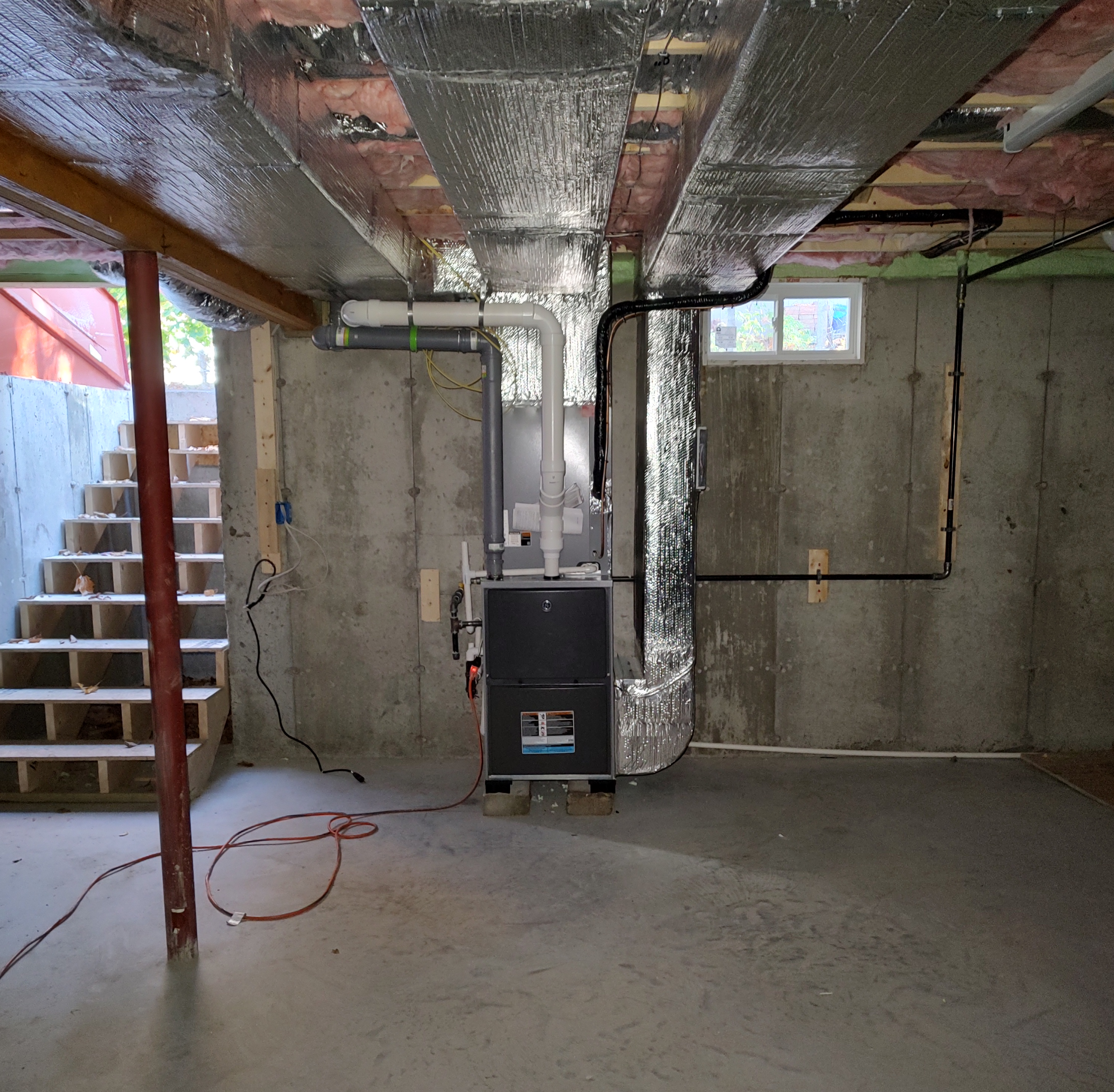 A new furnace installed in a basement with duct work coming out the top. It is very clean looking.